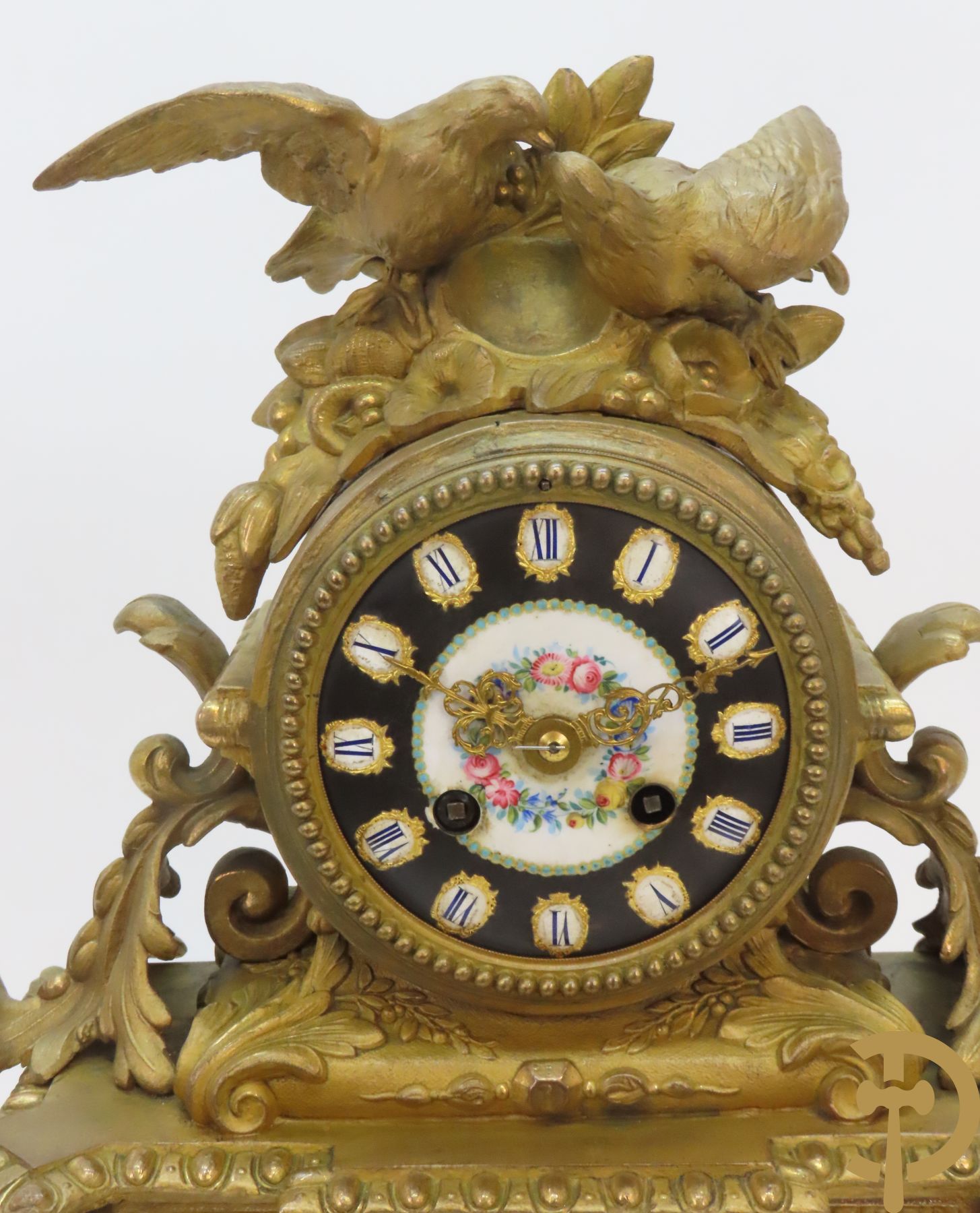 Vergulde pendule in zamak, wijzerplaat bezet met porseleinen plakkettes - bovenaan met vogelpaar, zijdelings met kariathyden houdende een bloementroffee - onder glazen stolp
