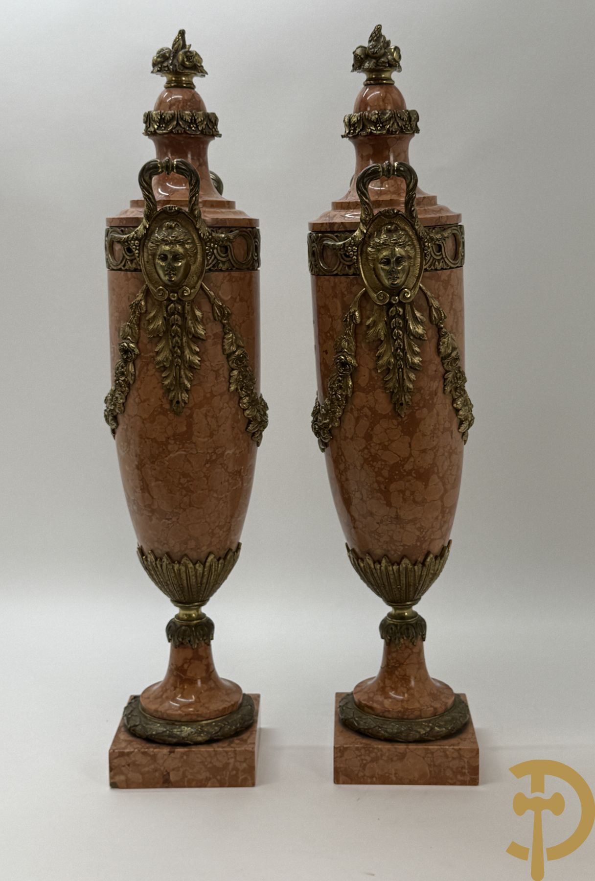 Paar oranje/rode marmeren cassolettes, zijdelings bezet met dameshoofden dragende een guirlande van bloemen - bovenaan met bloementroffee