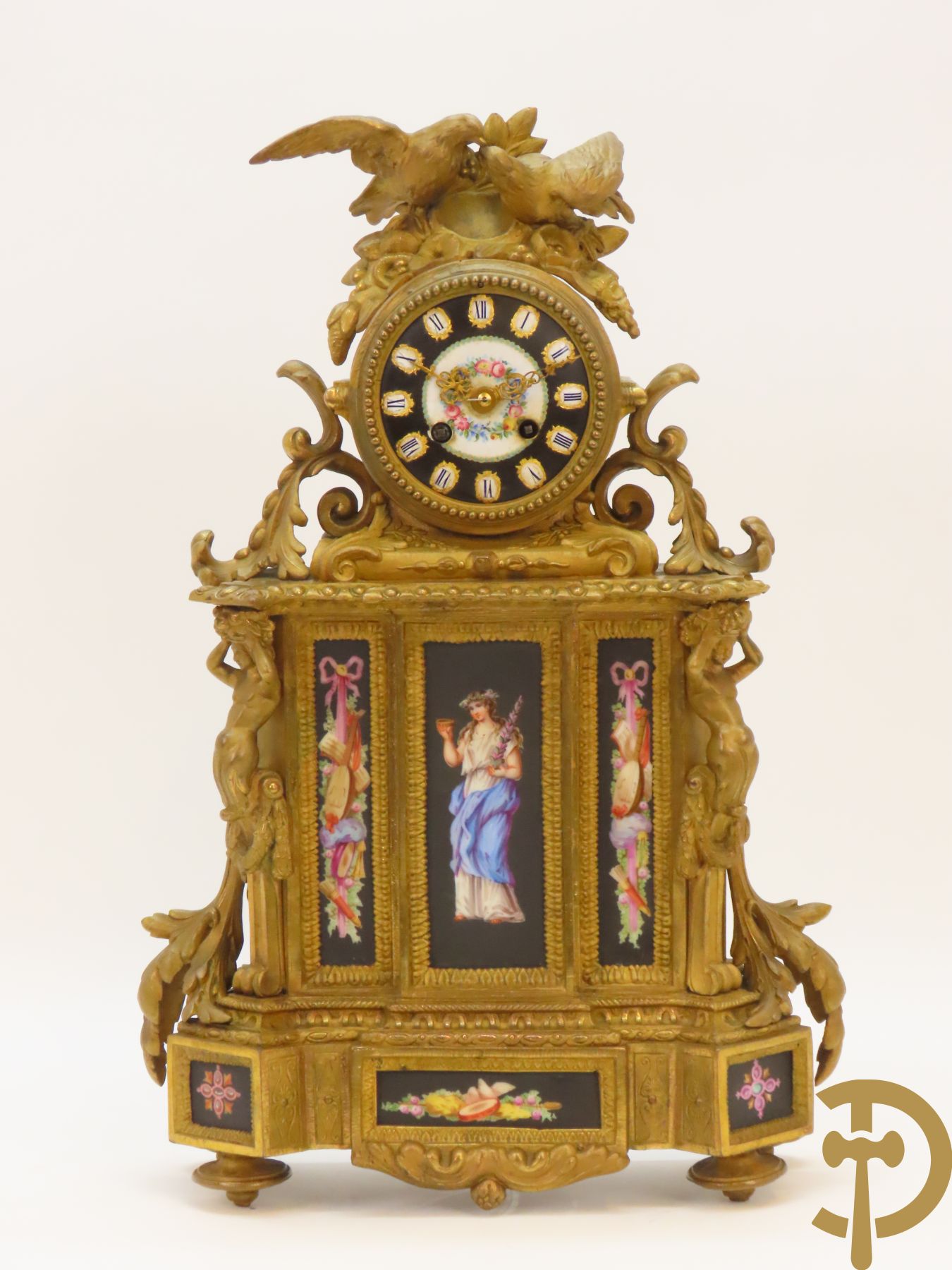 Vergulde pendule in zamak, wijzerplaat bezet met porseleinen plakkettes - bovenaan met vogelpaar, zijdelings met kariathyden houdende een bloementroffee - onder glazen stolp