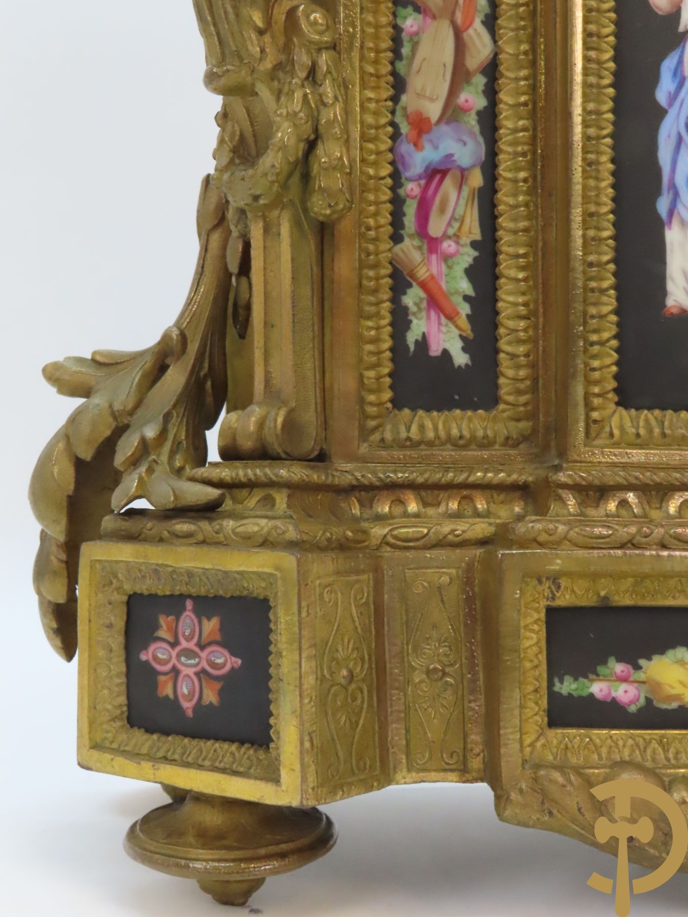 Vergulde pendule in zamak, wijzerplaat bezet met porseleinen plakkettes - bovenaan met vogelpaar, zijdelings met kariathyden houdende een bloementroffee - onder glazen stolp