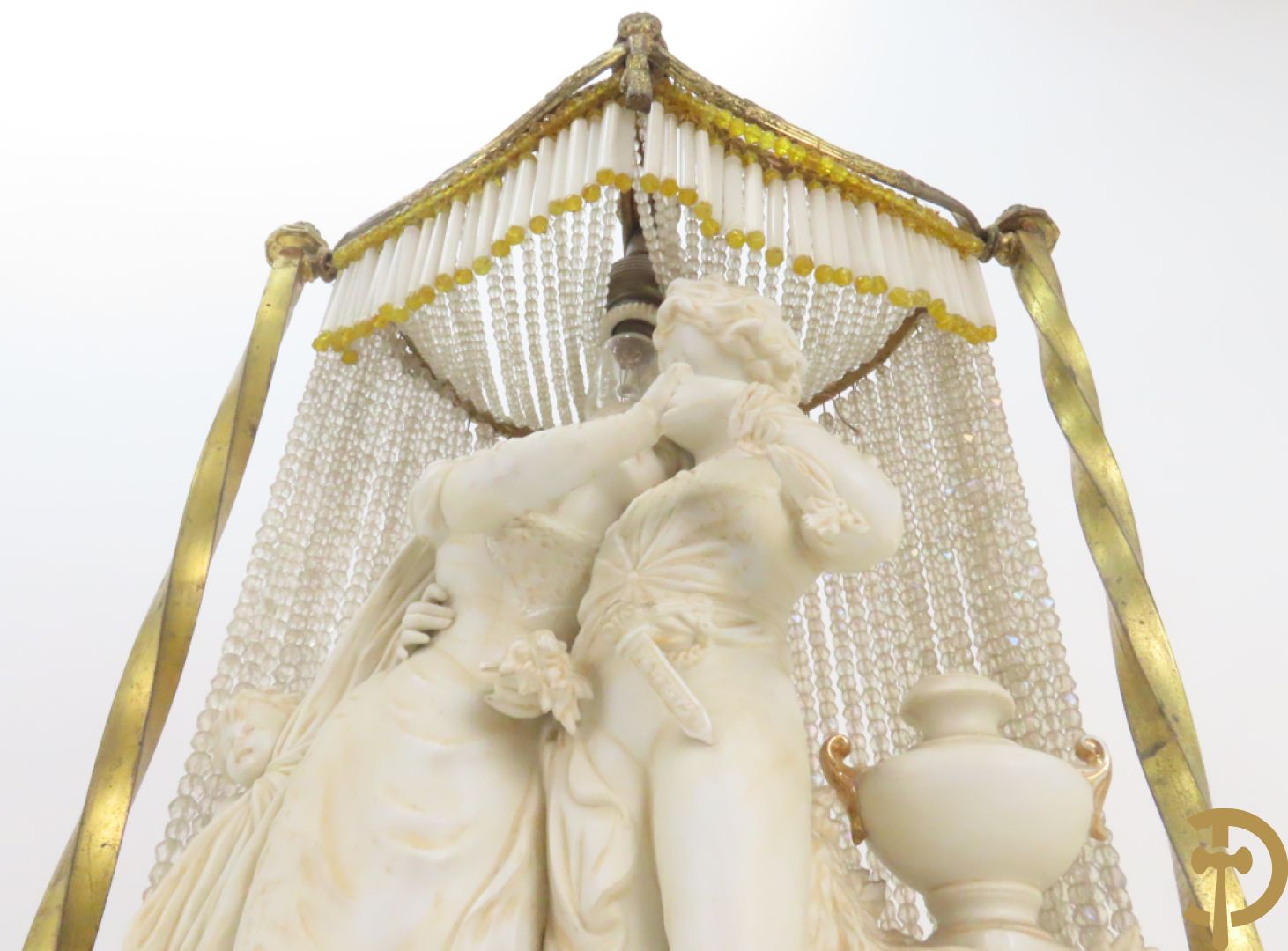 Lieftallig biscuit van romantisch koppel bij amfoor met kleine neergezeten cupido onder koperen baldakijn met kristallen belletjes