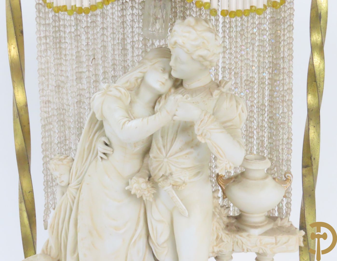 Lieftallig biscuit van romantisch koppel bij amfoor met kleine neergezeten cupido onder koperen baldakijn met kristallen belletjes