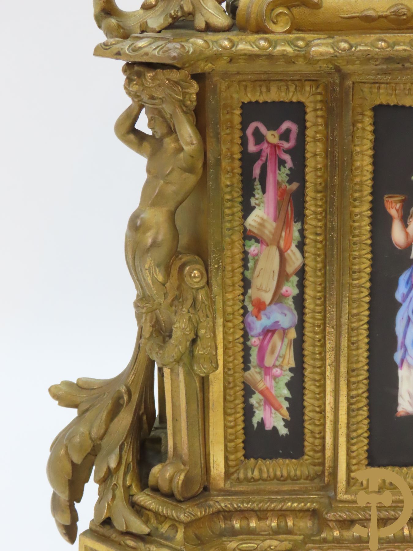 Vergulde pendule in zamak, wijzerplaat bezet met porseleinen plakkettes - bovenaan met vogelpaar, zijdelings met kariathyden houdende een bloementroffee - onder glazen stolp