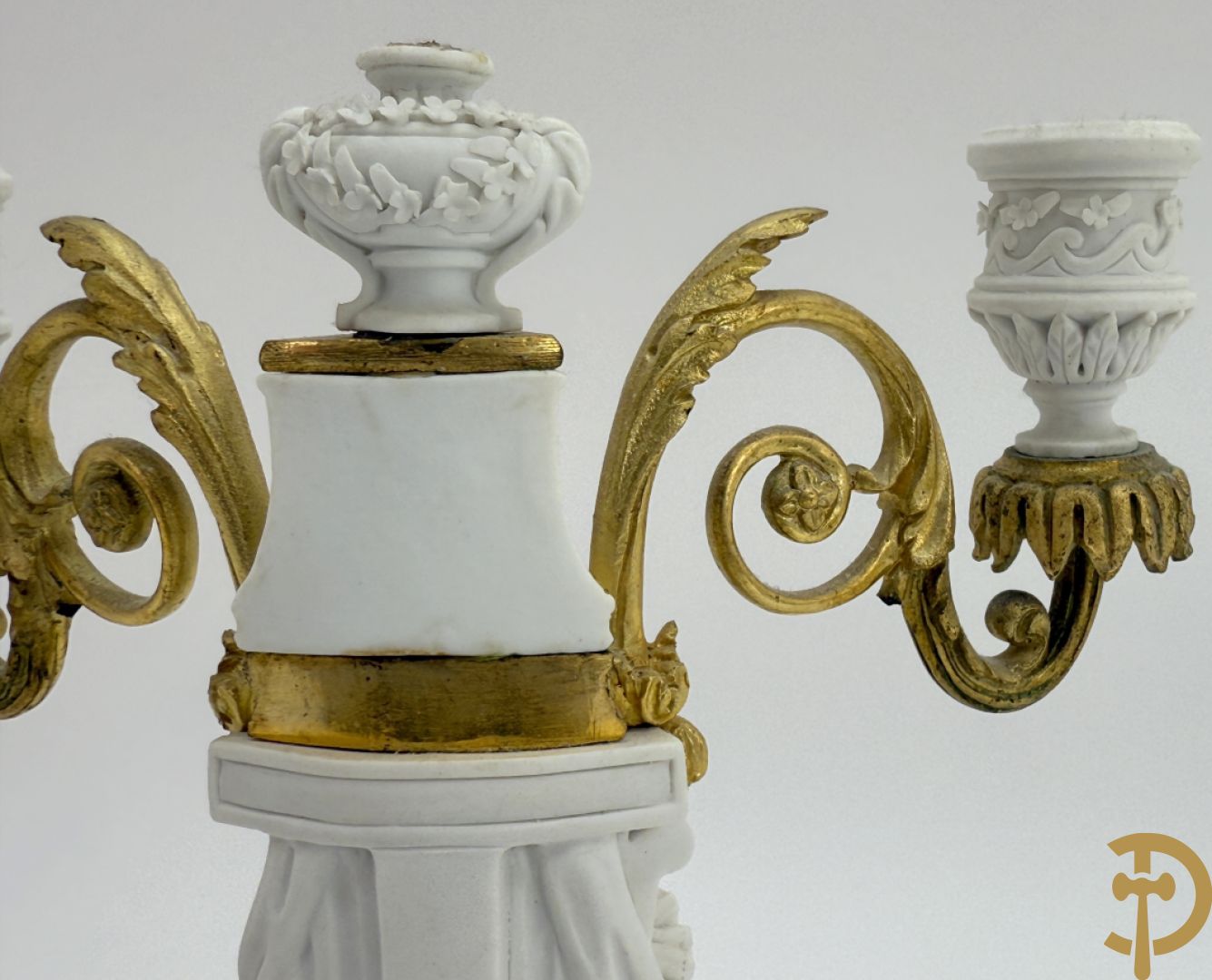 Driedelige porseleinen garnituur met bronsbeslag bestaande uit pendule met dame en amfoor geflankeerd door paar kandelaars bezet met personages