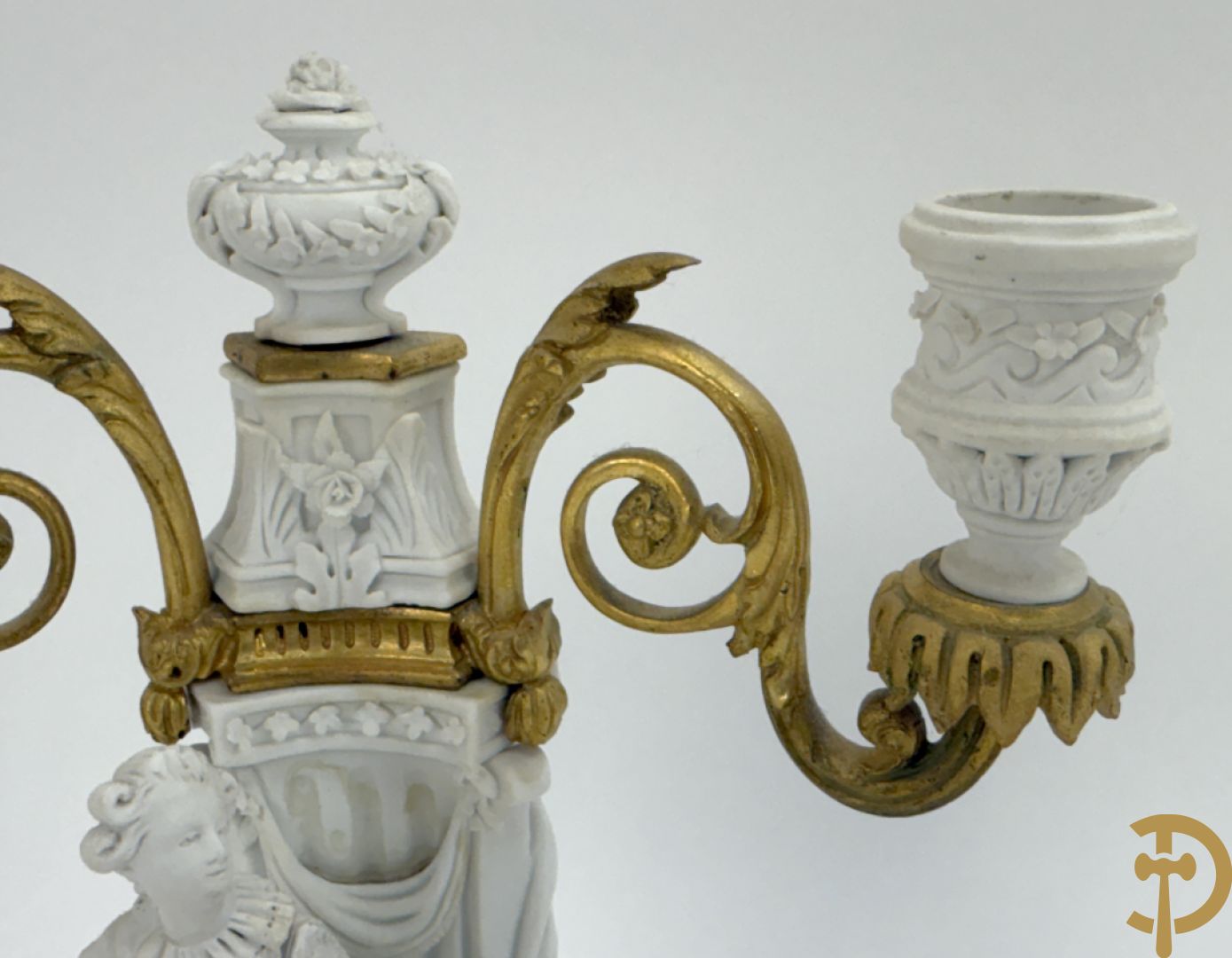 Driedelige porseleinen garnituur met bronsbeslag bestaande uit pendule met dame en amfoor geflankeerd door paar kandelaars bezet met personages