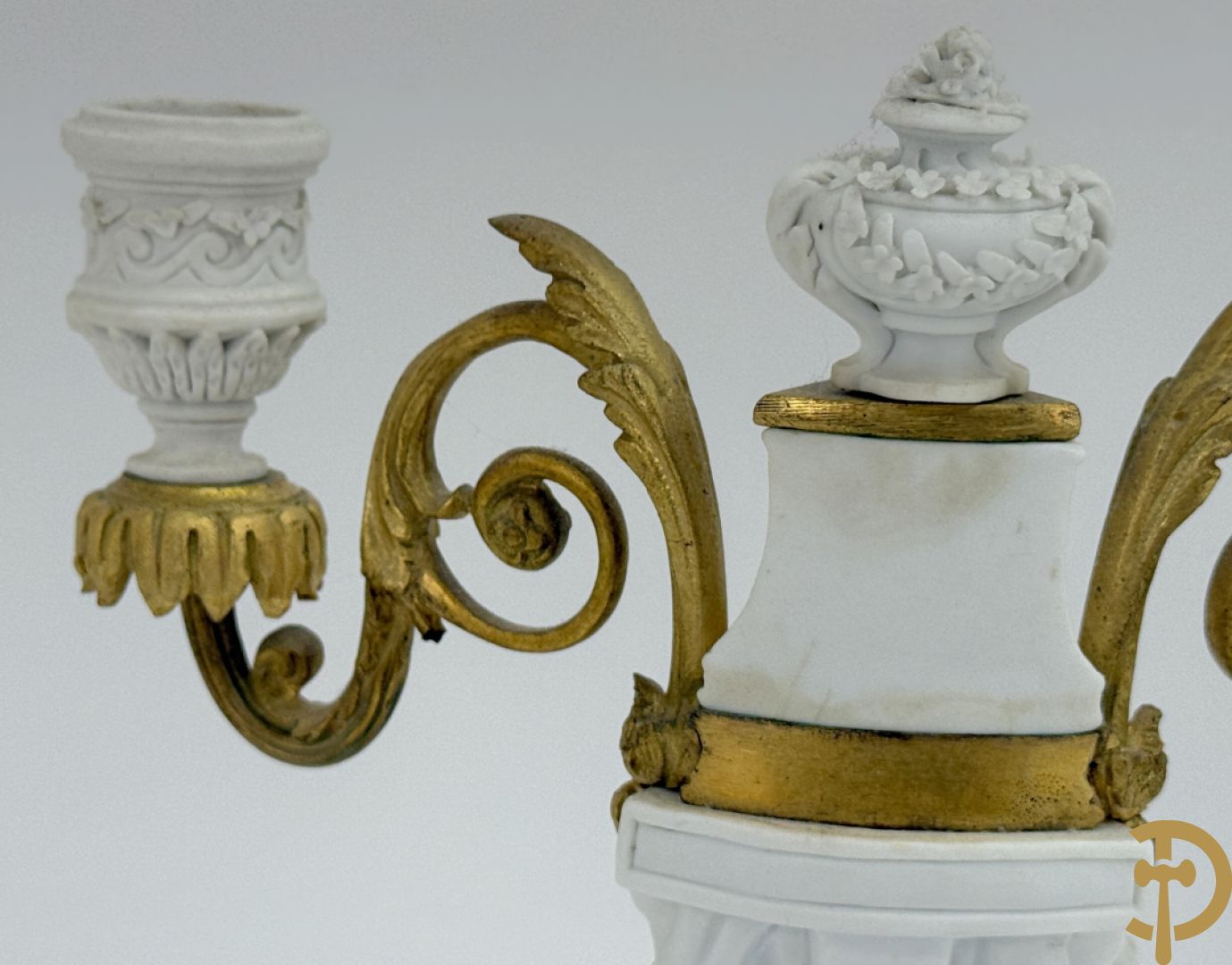 Driedelige porseleinen garnituur met bronsbeslag bestaande uit pendule met dame en amfoor geflankeerd door paar kandelaars bezet met personages