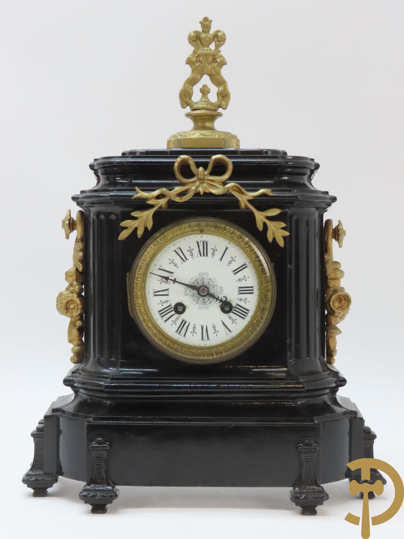 Gepatineerde gietijzeren pendule met bloemenmotieven en Louis XVI strik, bovenaan bekroond met ornament