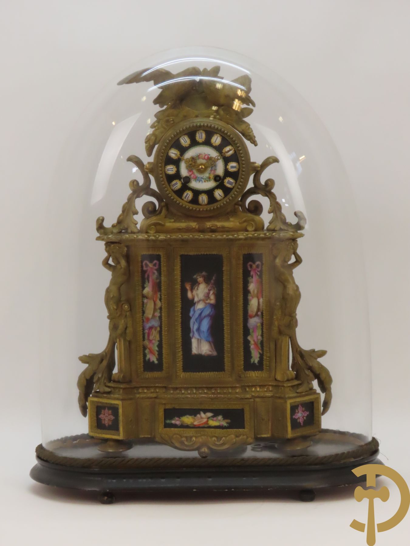 Vergulde pendule in zamak, wijzerplaat bezet met porseleinen plakkettes - bovenaan met vogelpaar, zijdelings met kariathyden houdende een bloementroffee - onder glazen stolp