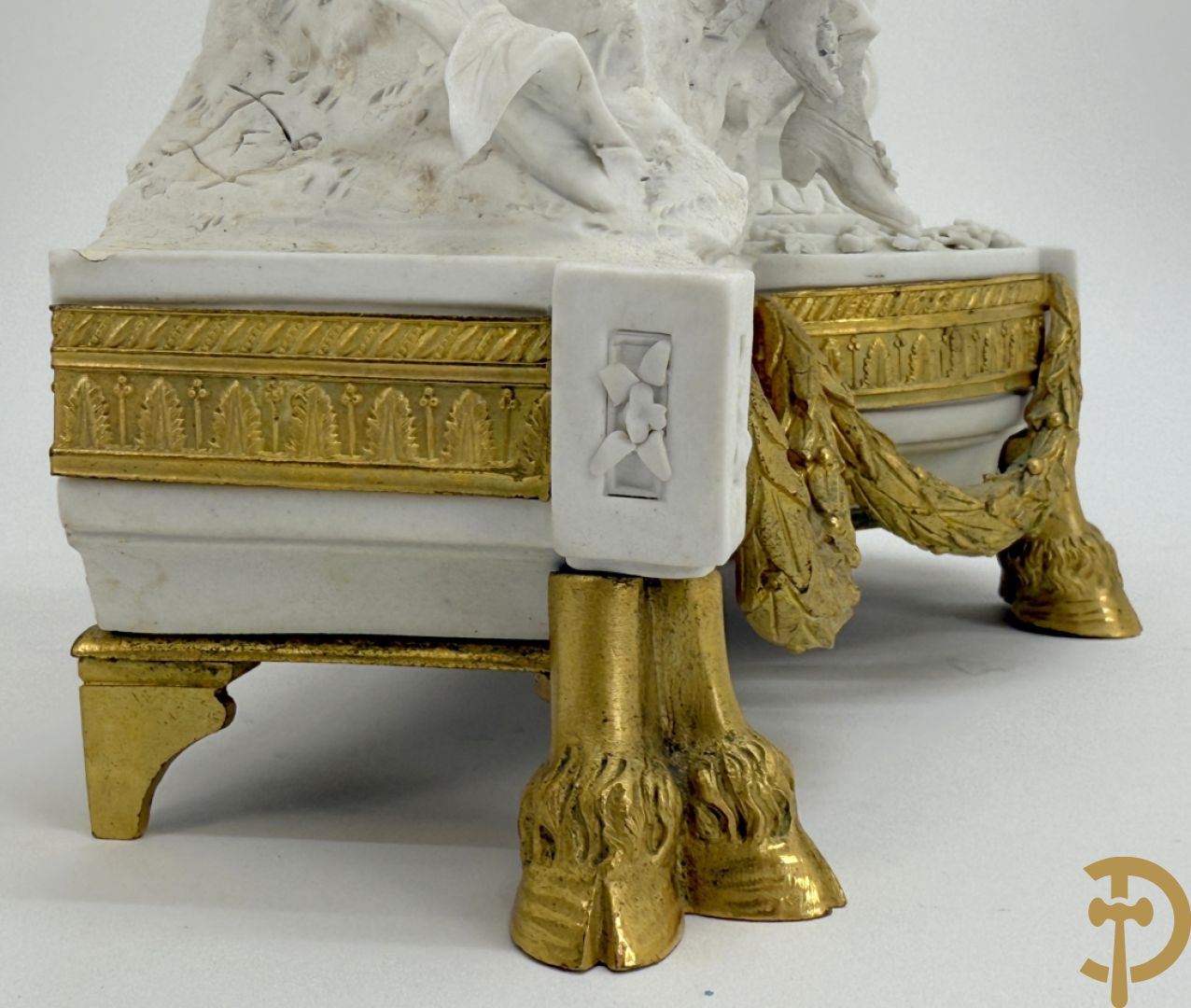 Driedelige porseleinen garnituur met bronsbeslag bestaande uit pendule met dame en amfoor geflankeerd door paar kandelaars bezet met personages