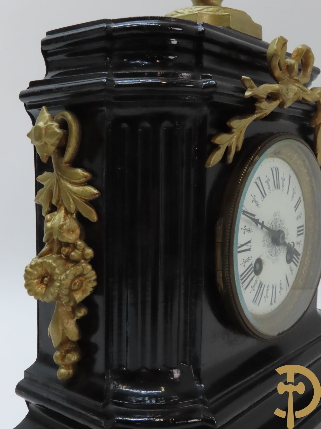 Gepatineerde gietijzeren pendule met bloemenmotieven en Louis XVI strik, bovenaan bekroond met ornament