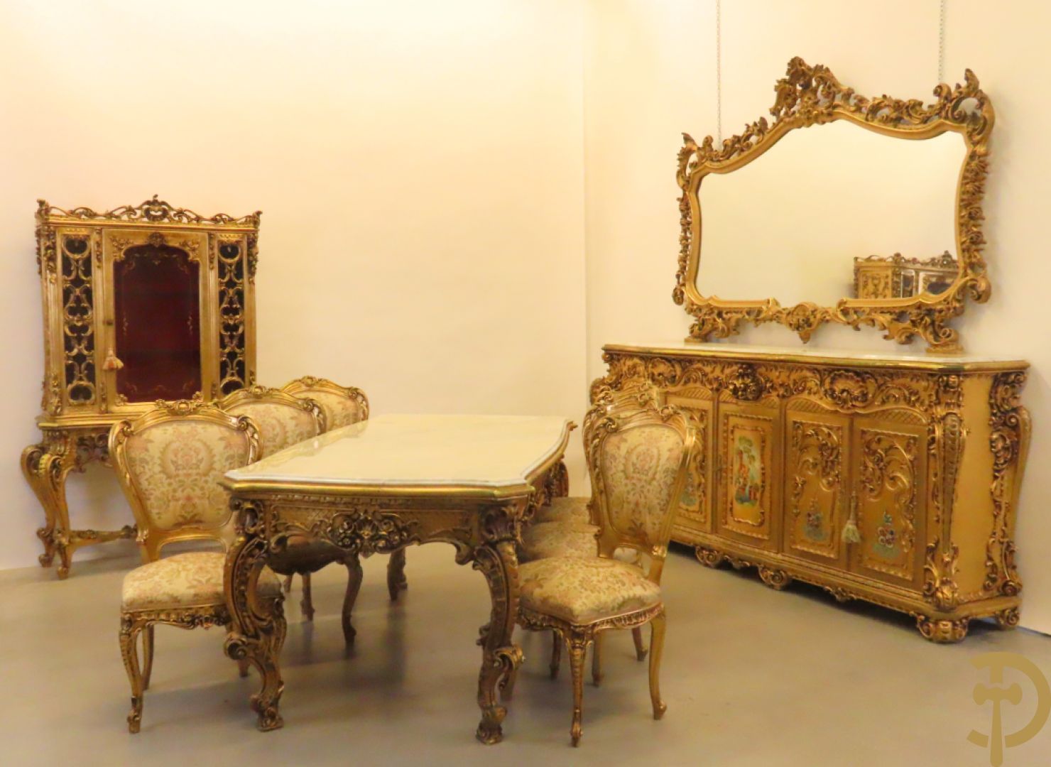 Uitzonderlijke vergulde Louis XV eetkamer bestaande uit vijfdeursdressoir met voluutvormige accanthusranken en rocailles, beschilderd met bloemenmotieven en centraal tafererel met hoornen des overvloeds + bijhorende spiegel vergulde tafel op voluutvormige poten met zes bijhorende stoelen + vitrine met accanthusranken en centrale deur, op voluutvormige poten