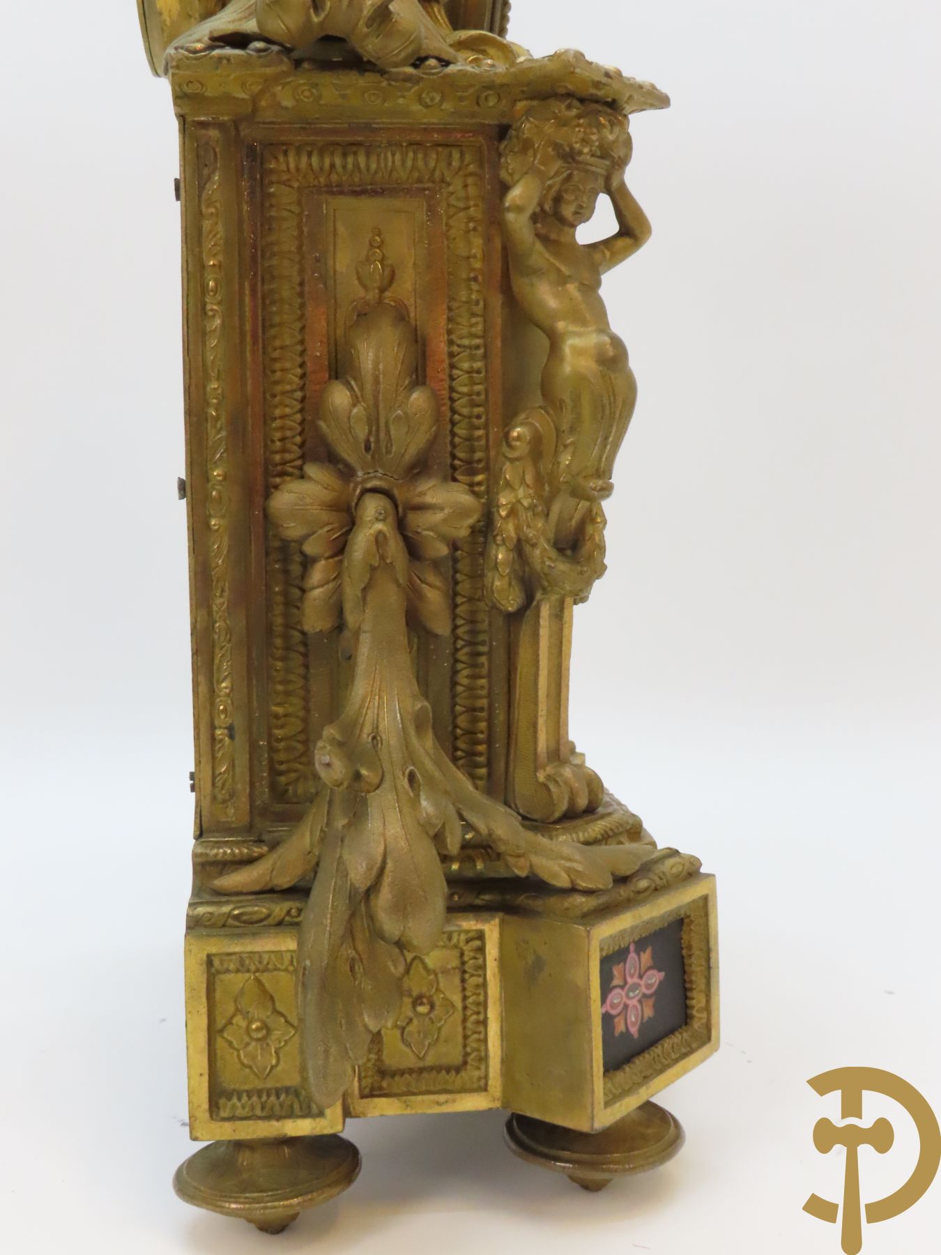 Vergulde pendule in zamak, wijzerplaat bezet met porseleinen plakkettes - bovenaan met vogelpaar, zijdelings met kariathyden houdende een bloementroffee - onder glazen stolp