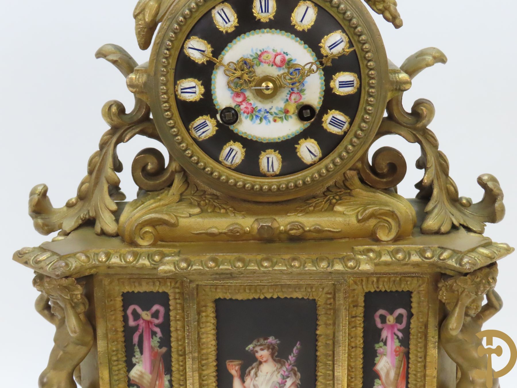 Vergulde pendule in zamak, wijzerplaat bezet met porseleinen plakkettes - bovenaan met vogelpaar, zijdelings met kariathyden houdende een bloementroffee - onder glazen stolp