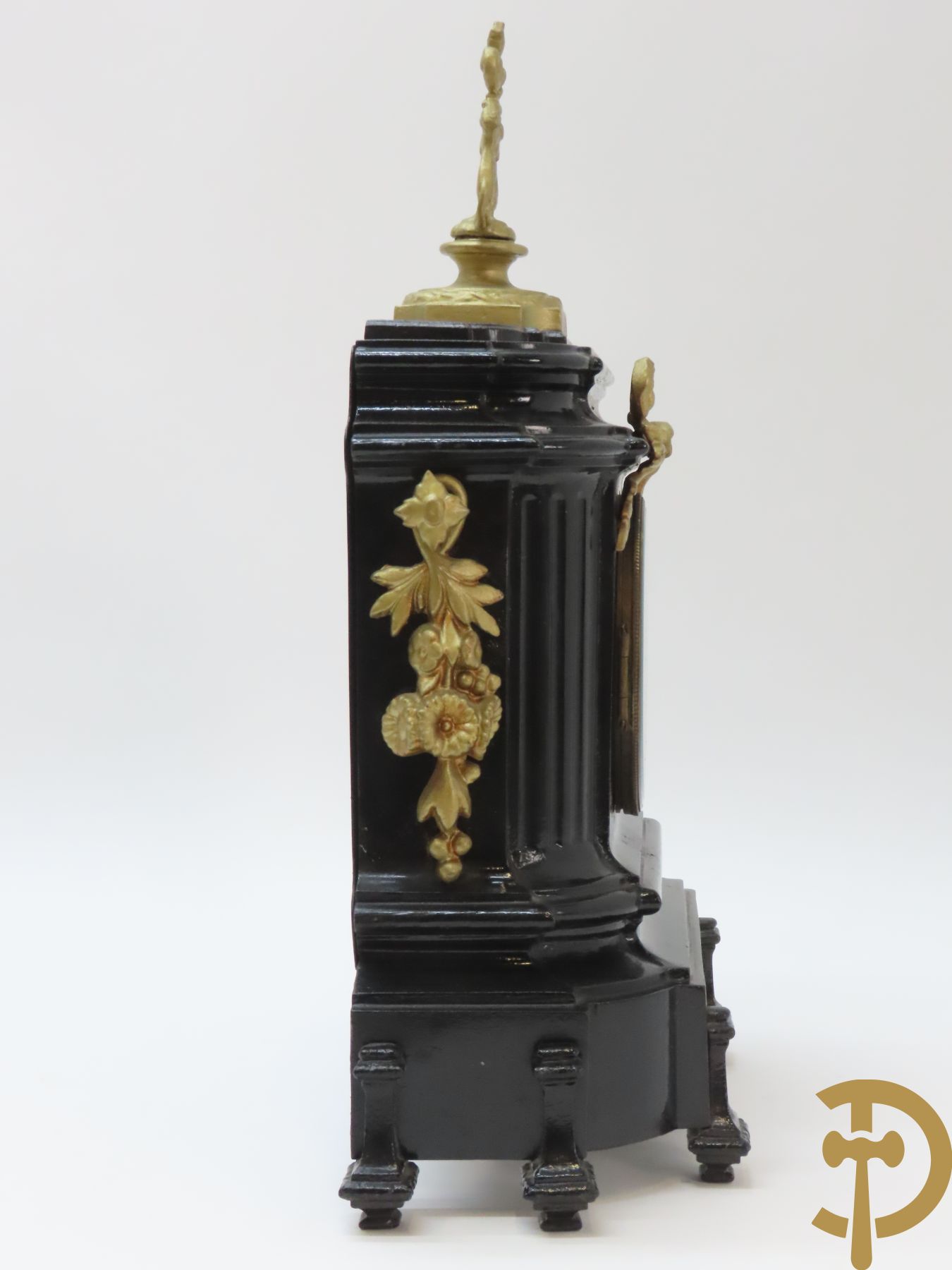 Gepatineerde gietijzeren pendule met bloemenmotieven en Louis XVI strik, bovenaan bekroond met ornament