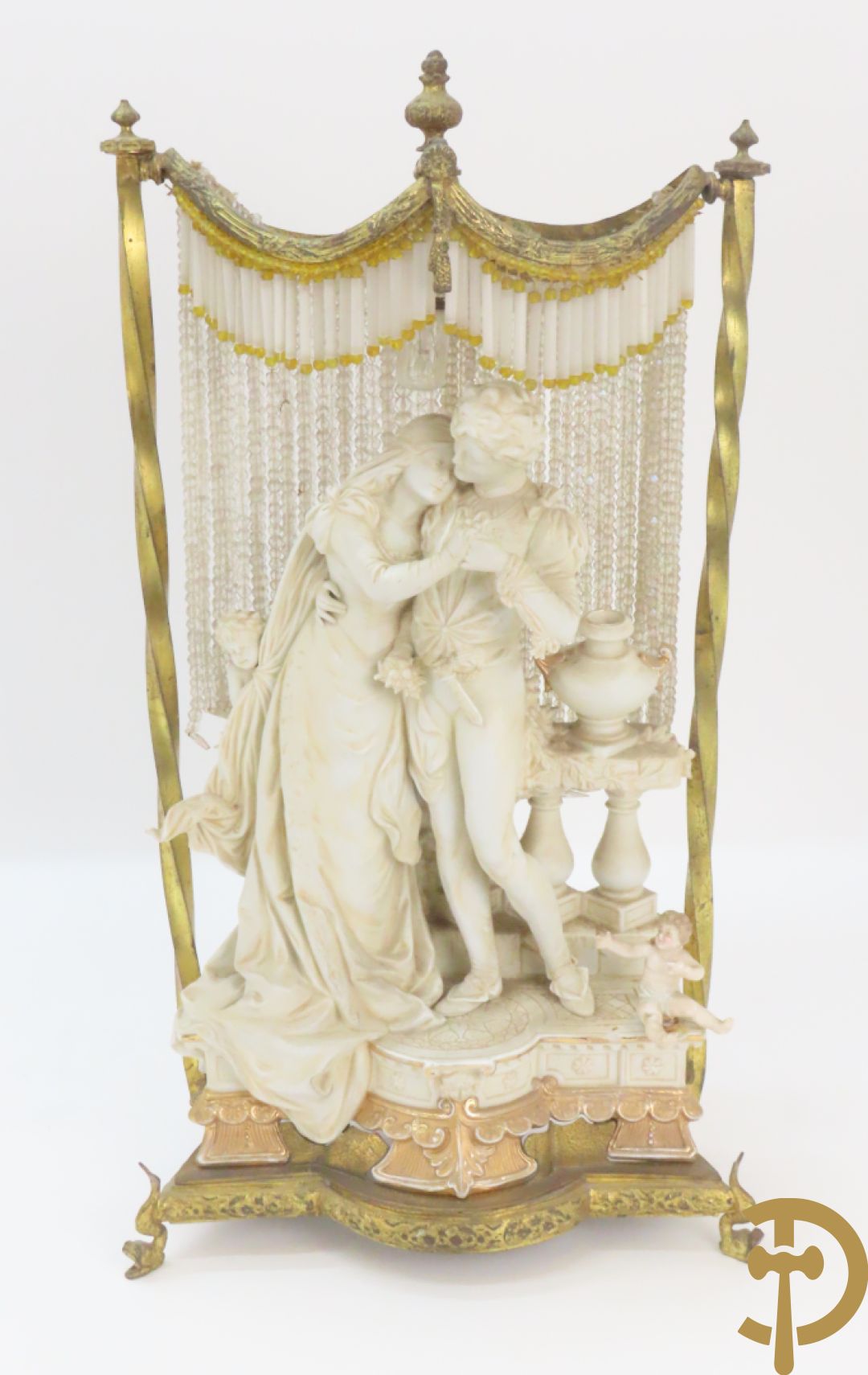 Lieftallig biscuit van romantisch koppel bij amfoor met kleine neergezeten cupido onder koperen baldakijn met kristallen belletjes