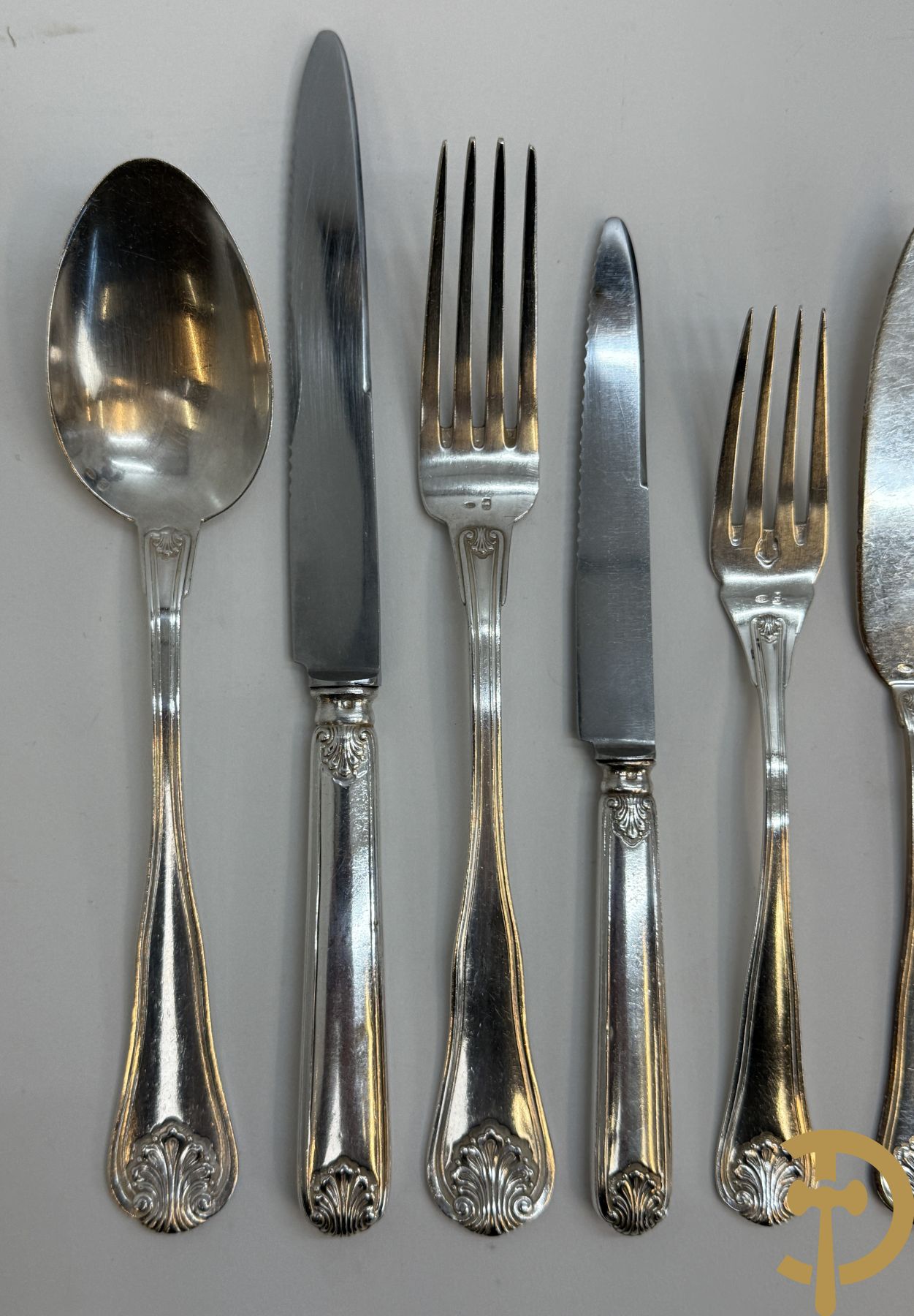 Massief zilveren bestek Wolfers bestaande uit 12 vorken (979 gram), 12 lepels (1028 gram), 11 messen, 12 visvorken (553 gram), 12 vismessen (690 gram), 12 dessertmessen, 10 koffielepels (296 gram), 12 ijslepels (369 gram), 3 botermesjes en scheplepeltje (165 gram), 5  grote stukken (samen 557 gram) waarvan slacouvert, 2 taartscheppen en wildvork + sauslepel met zelfde decor maar Metal Blanc