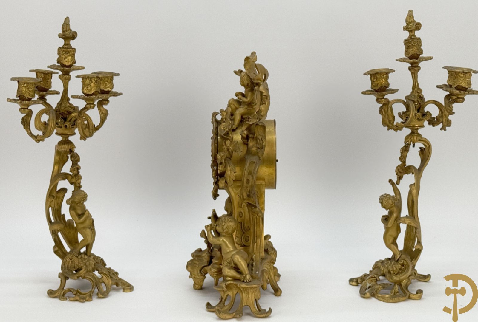 Driedelige vuurvergulde bronzen garnituur, Louis XV stijl, bestaande uit middenstuk met klok omgeven door musicerende cupido