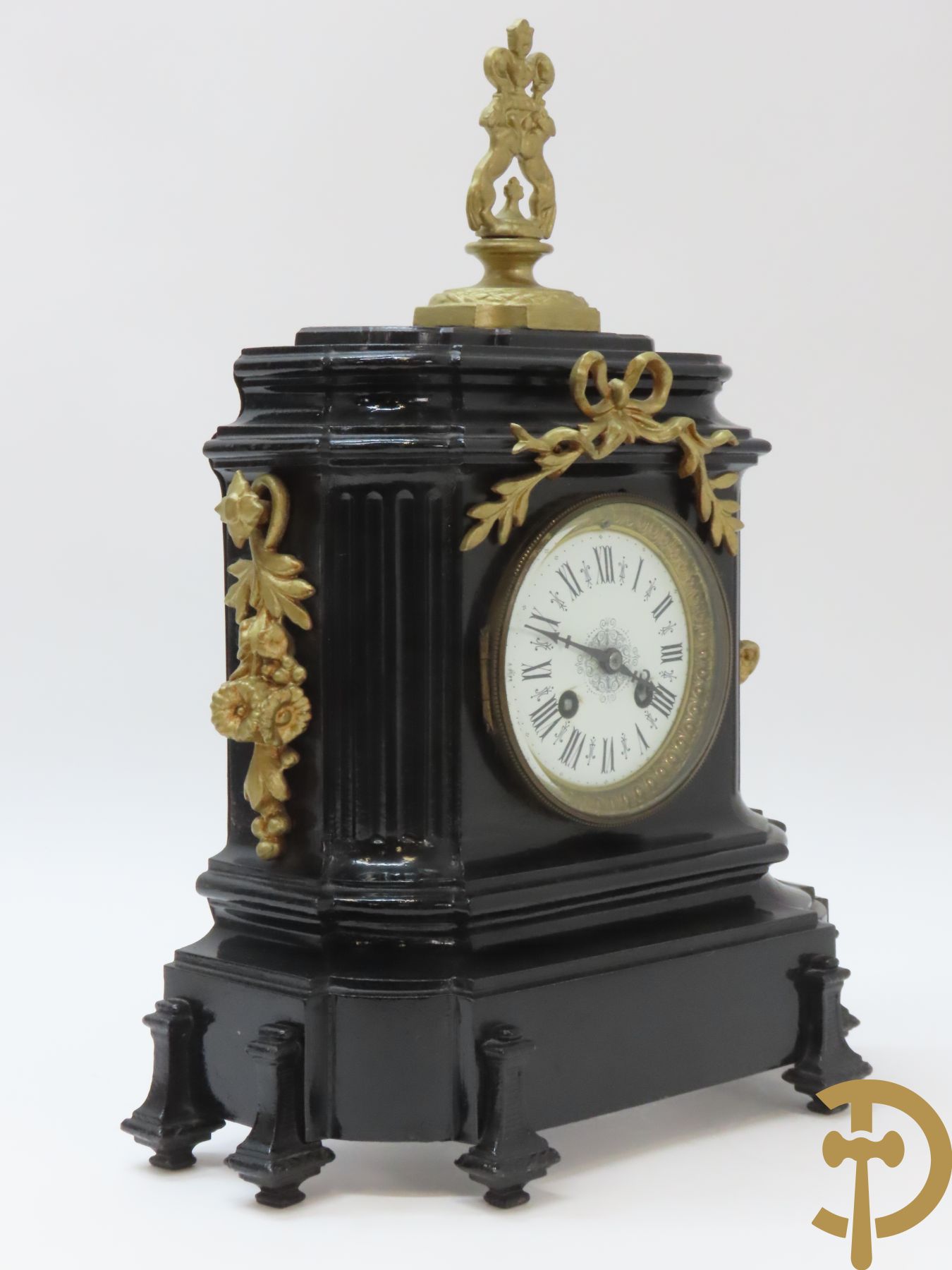 Gepatineerde gietijzeren pendule met bloemenmotieven en Louis XVI strik, bovenaan bekroond met ornament