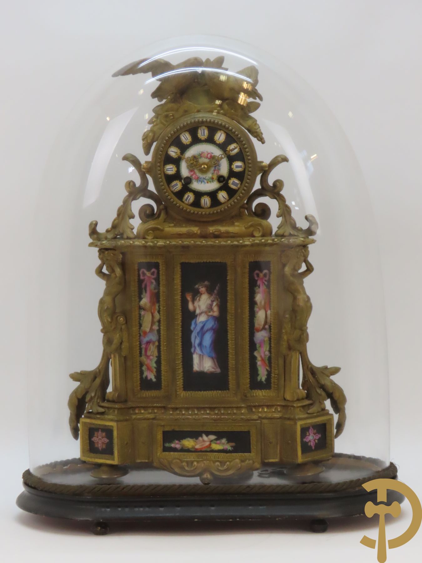Vergulde pendule in zamak, wijzerplaat bezet met porseleinen plakkettes - bovenaan met vogelpaar, zijdelings met kariathyden houdende een bloementroffee - onder glazen stolp