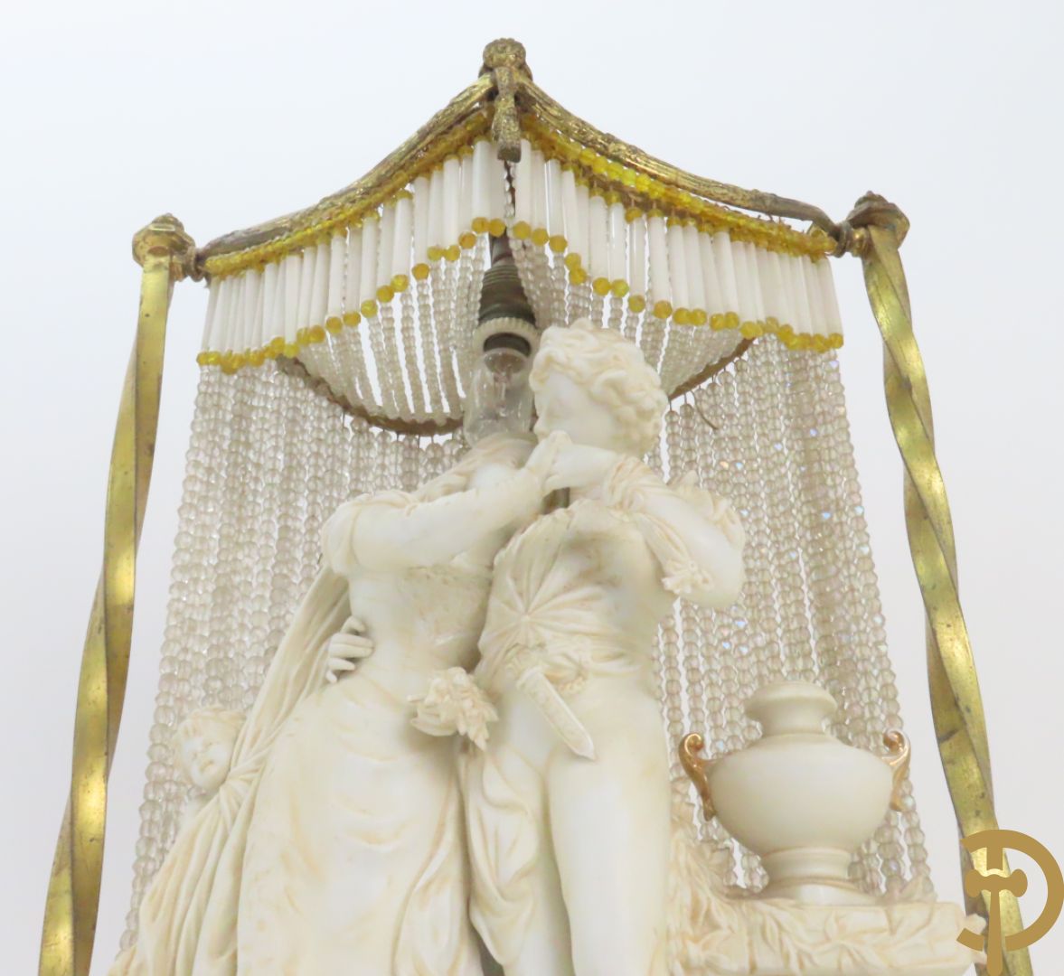 Lieftallig biscuit van romantisch koppel bij amfoor met kleine neergezeten cupido onder koperen baldakijn met kristallen belletjes