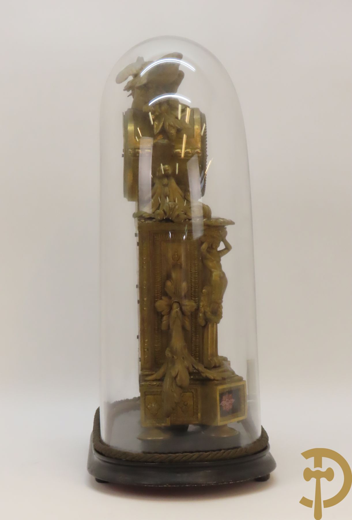 Vergulde pendule in zamak, wijzerplaat bezet met porseleinen plakkettes - bovenaan met vogelpaar, zijdelings met kariathyden houdende een bloementroffee - onder glazen stolp