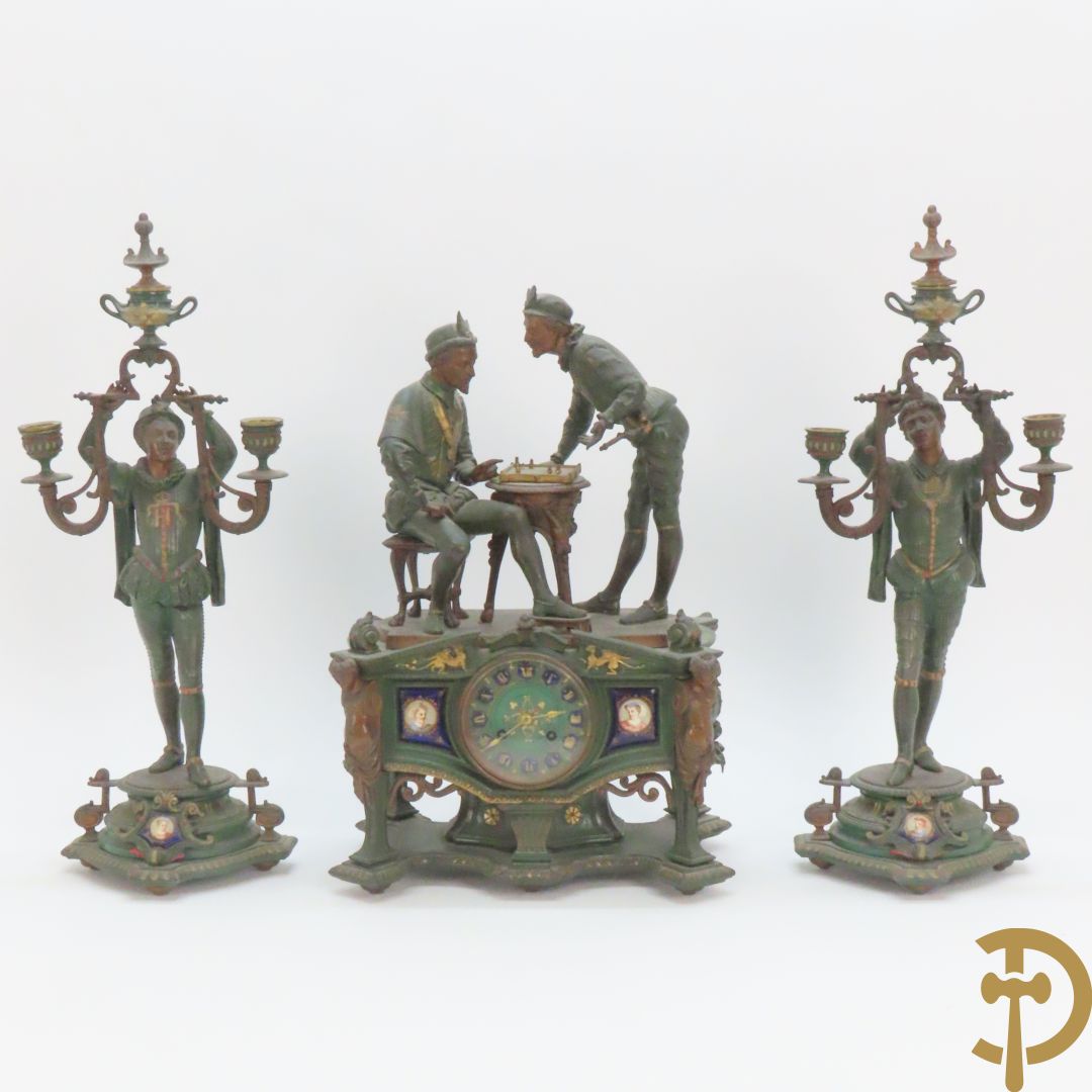 Driedelige kunstbronzen garnituur bestaande uit pendule met paar schakende edelheren, bezet met kariatiden - geflankeerd door paar driearmige kandelaars gehouden door 2 edelheren