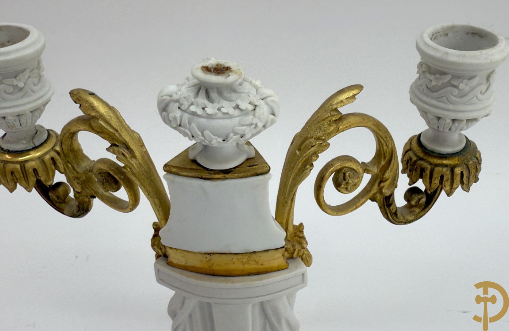 Driedelige porseleinen garnituur met bronsbeslag bestaande uit pendule met dame en amfoor geflankeerd door paar kandelaars bezet met personages